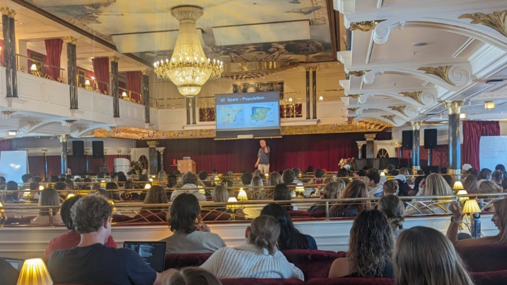 A cruise ship theatre full of students listening to a professor give a lecture.