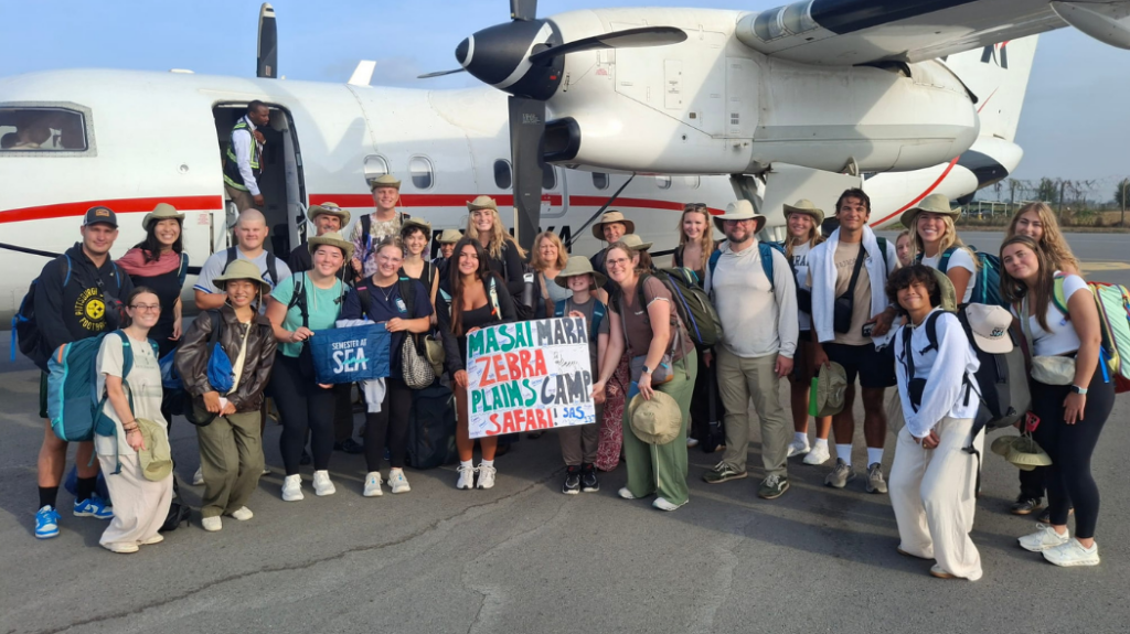 A group posing in front of an airplane, holding signs that say "Semester at Sea"
