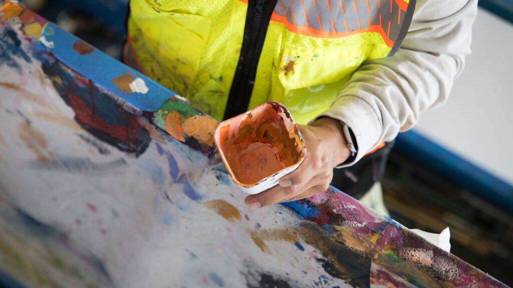 Armando Silva's hand holding orange paint in a square container