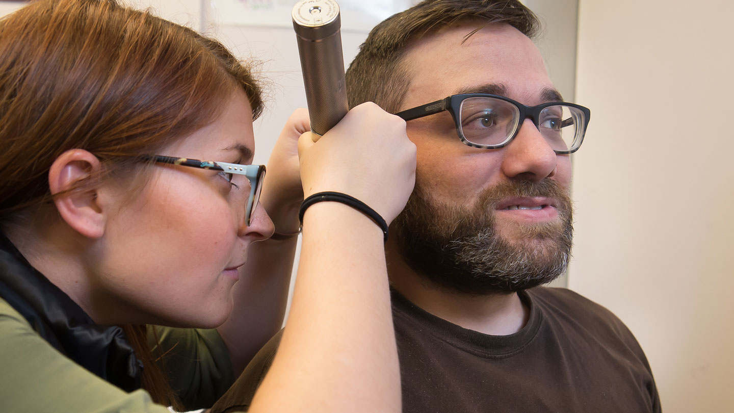 Speech-Language Pathology student examining a patient's ear.