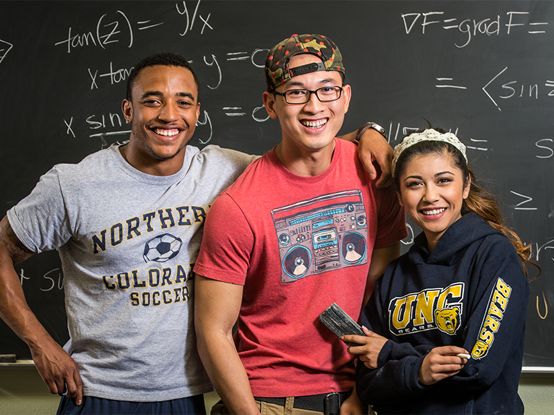 Three students standing in front of a chalkboard with mathematical equations on it.