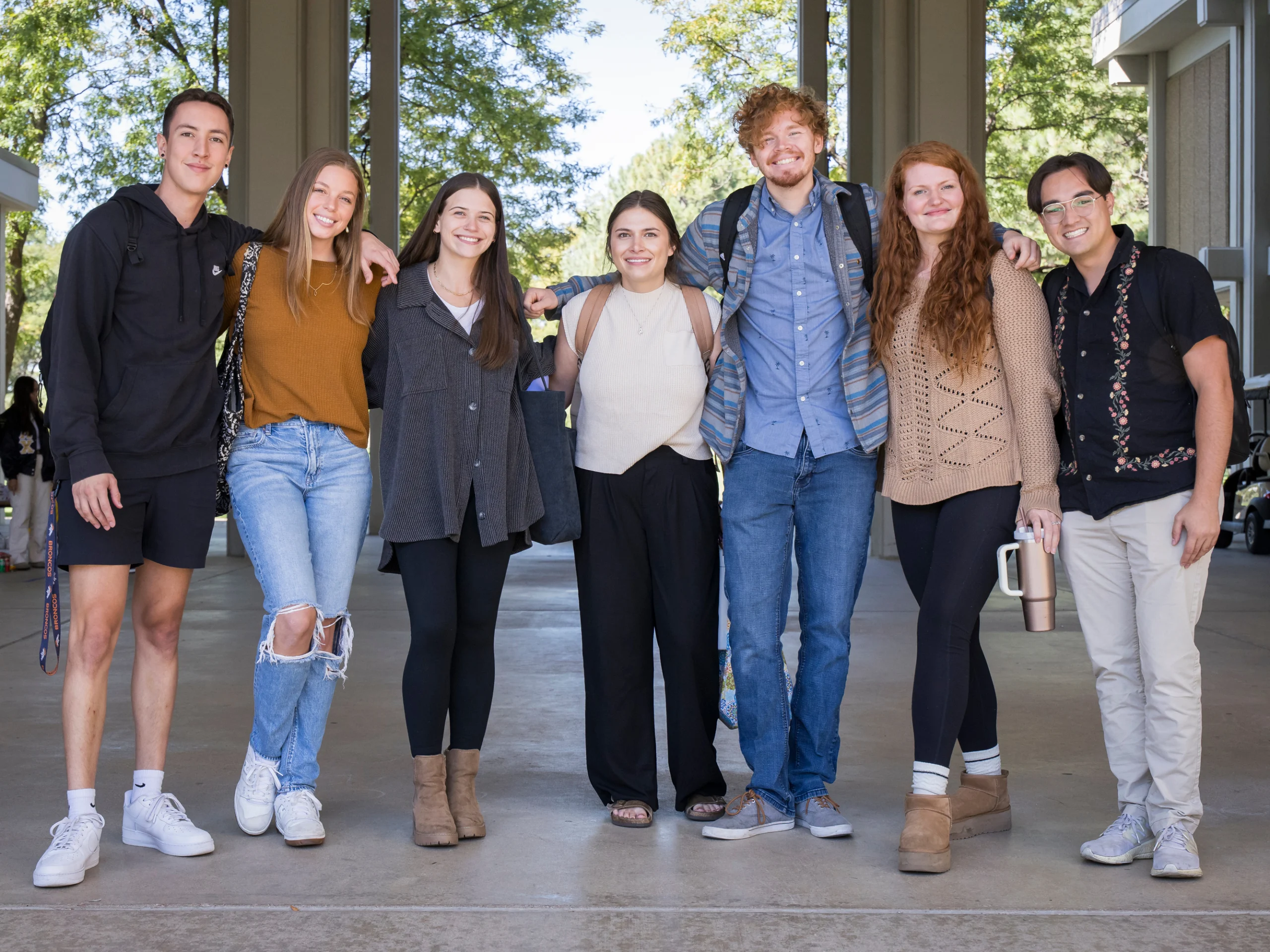 Seven students posing for a photo under the McKee breezeway with a backdrop of green trees in the background.