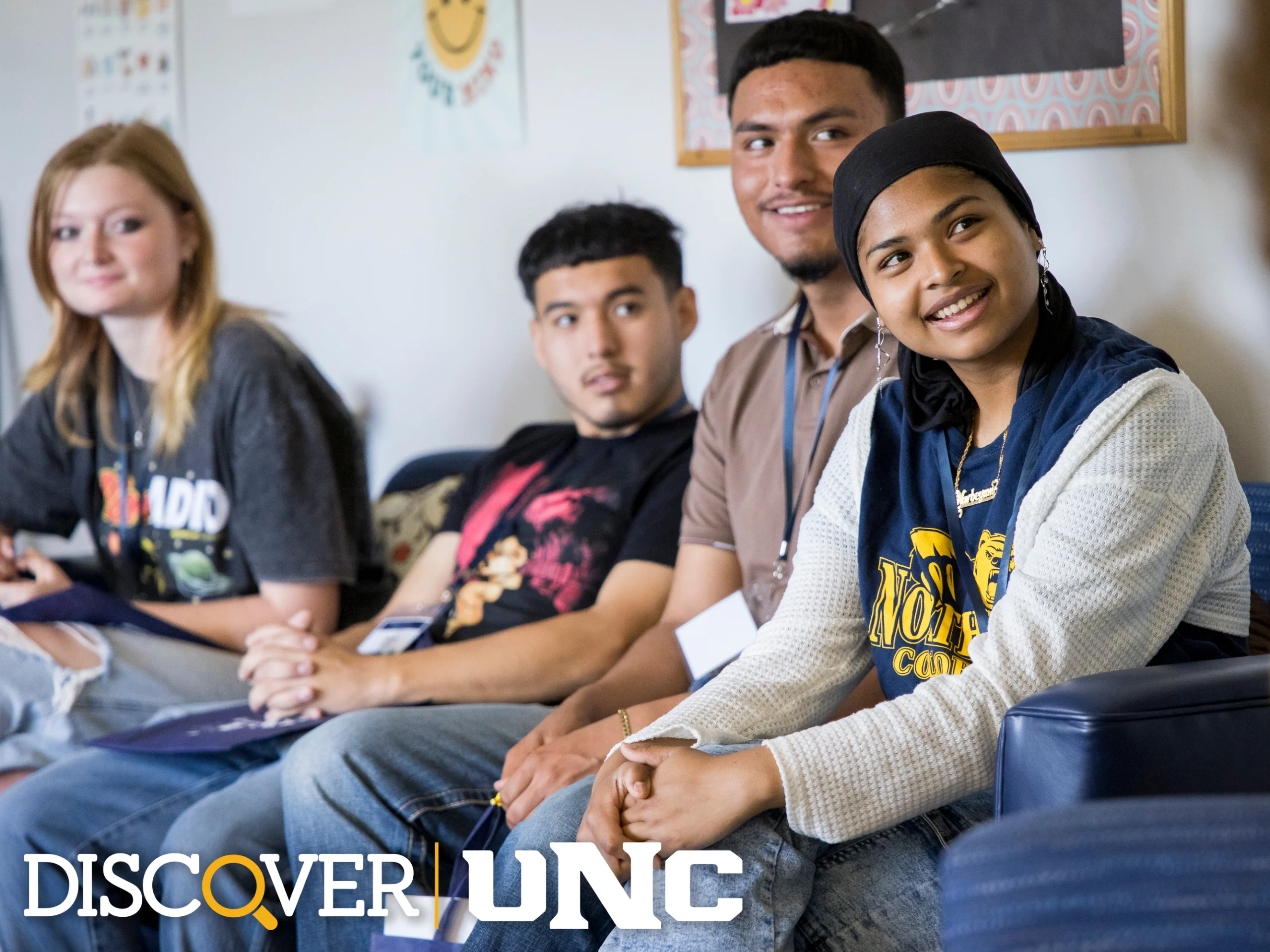 Four students sitting in a hallway while visiting campus with the Discover UNC logo in the lower right corner of the photo.