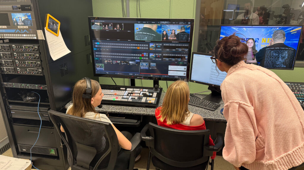 two middle school students sitting in front of a switch board in a control room