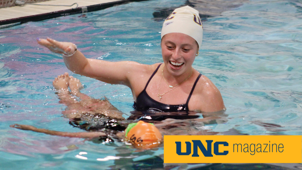 A UNC swim team member helping a young child float in the pool.