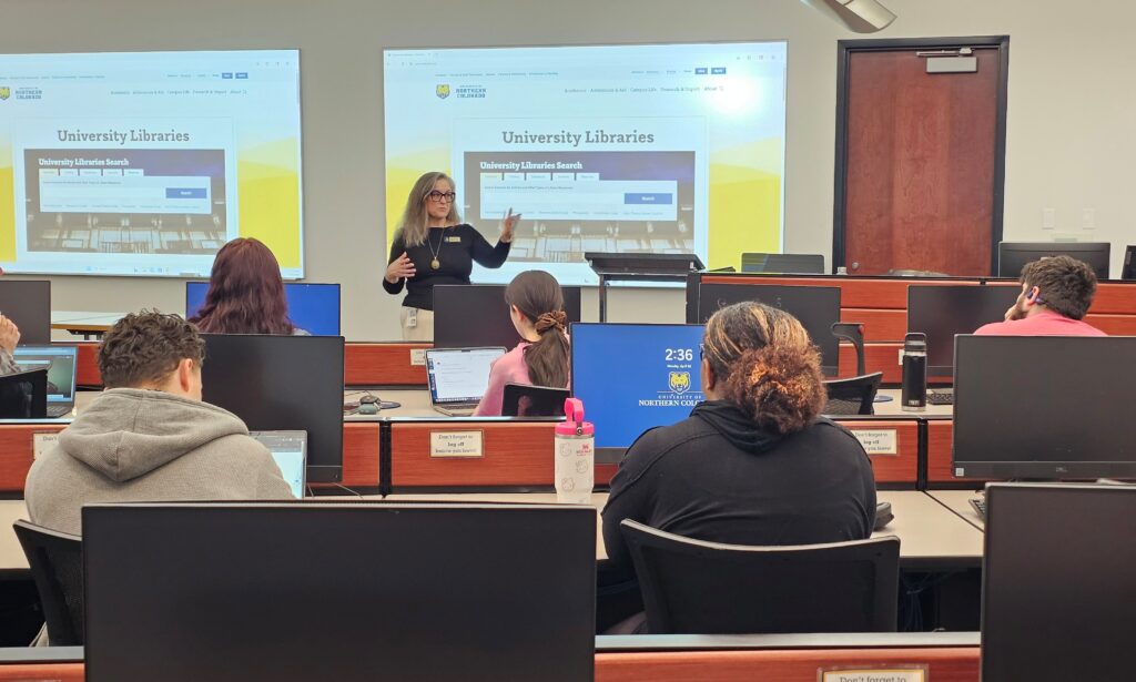 A librarian stands at the front of Michener 303 talking to a group of students who are sitting in rows at computers