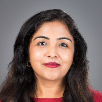 Headshot of a woman with long dark hair and brown eyes, wearing a red top against a gray background