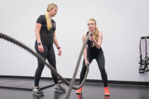 Student personal trainer encouraging student client who is using battle ropes.