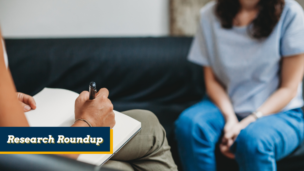 A close-up, over-the-shoulder shot of a counselor writing in a notebook, with a person sitting on a couch in front of them.
