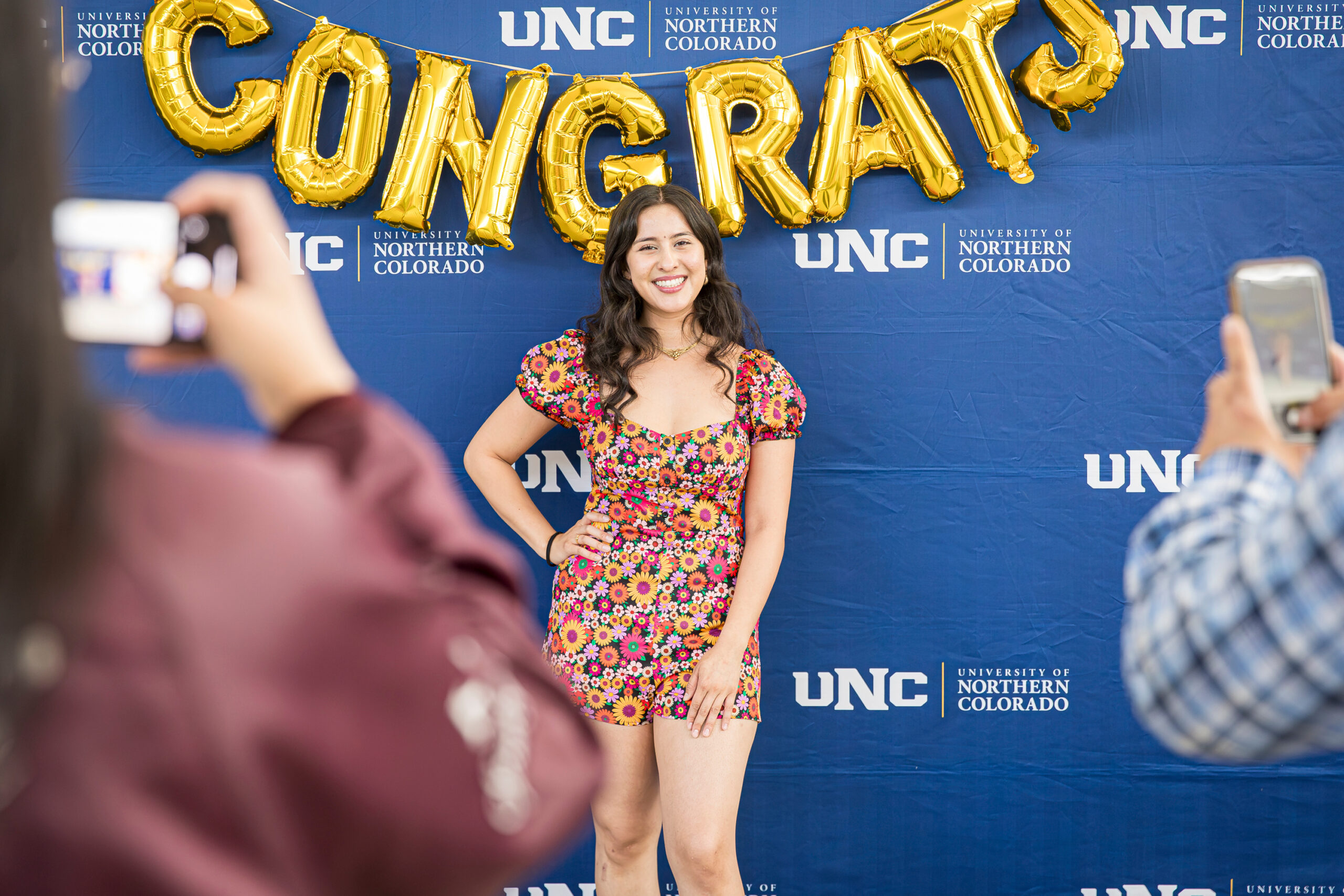 Student posing in front of a UNC backdrop at a graduation ceremony