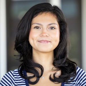 A person with long dark wavy hair smiles gently while wearing a navy and white striped top.