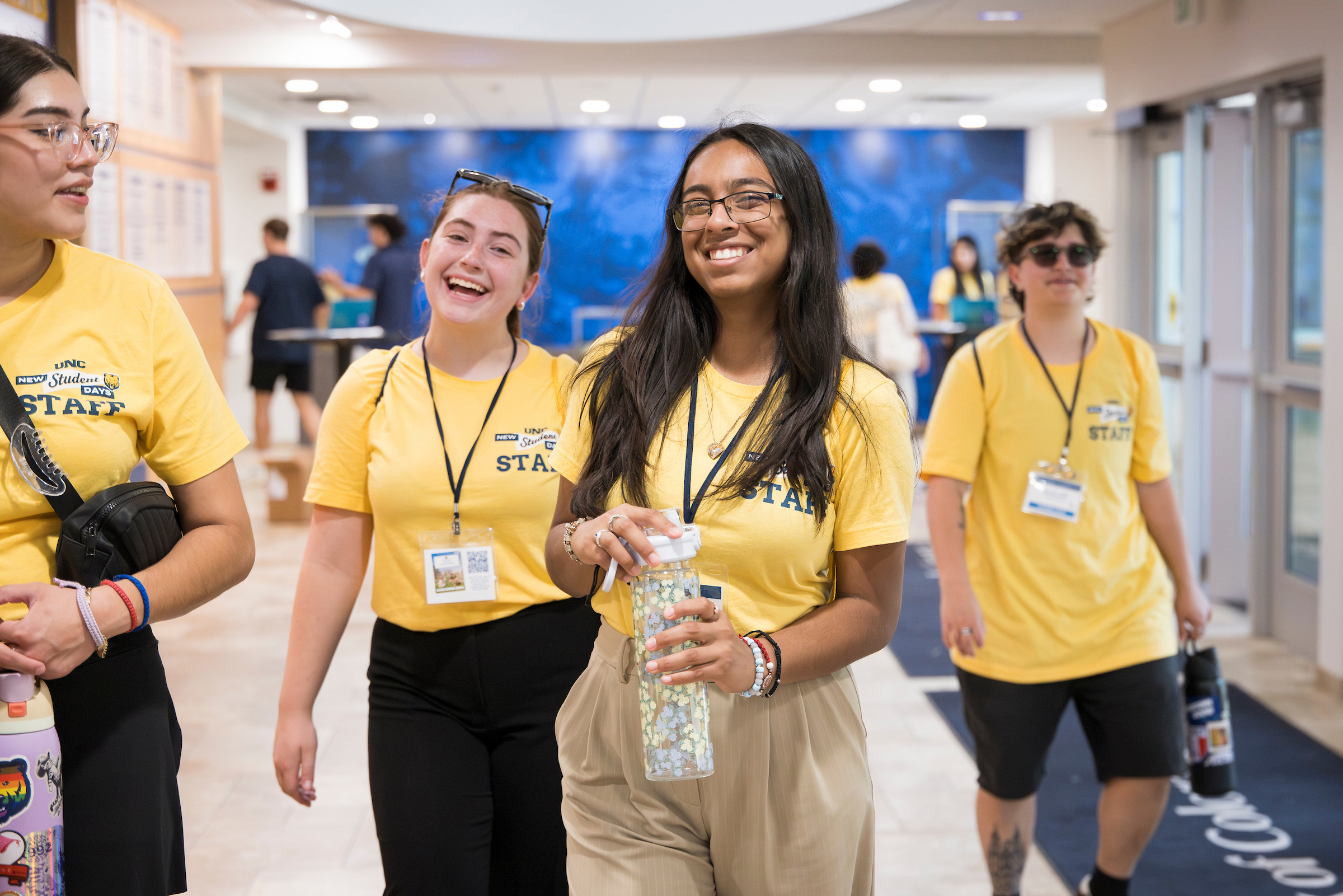 UNC New Student Days staff members in yellow shirts smile together in a campus lobby.