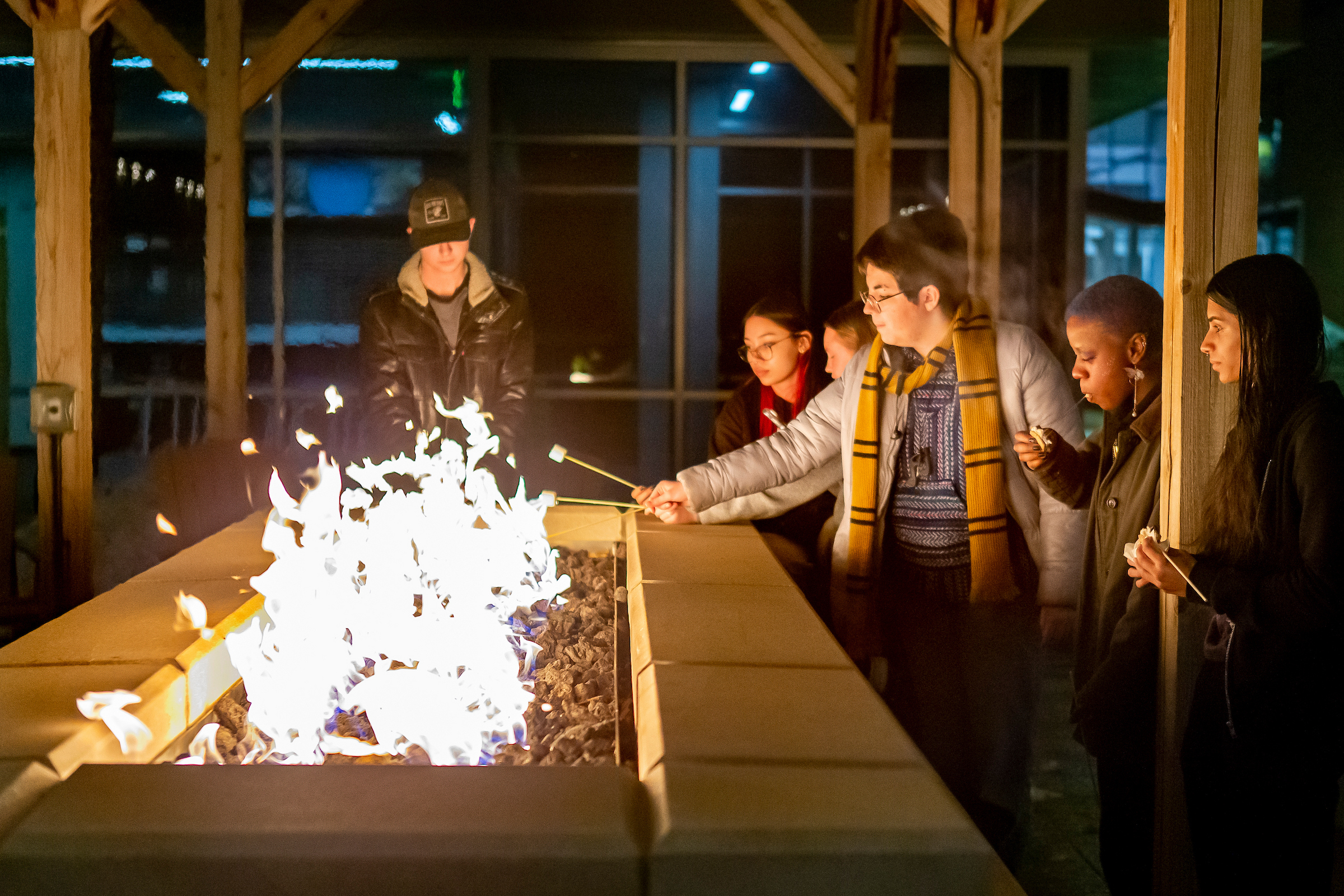 Students roast marshmallows over an outdoor fire pit at night during UNC’s Winter Welcome.