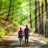 Two people walk down a path in the woods with backpacks