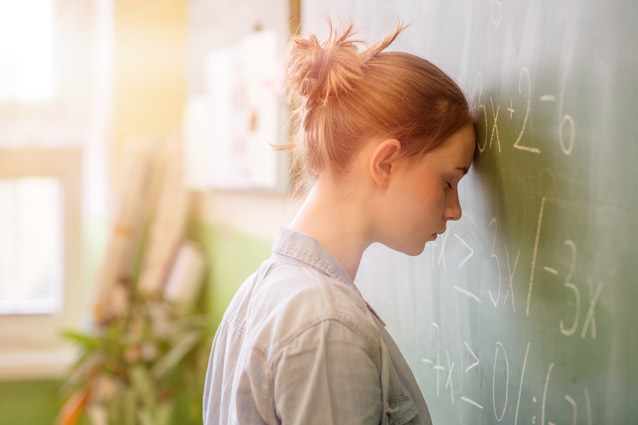 A young woman rests her head against a chalkboard. She is defeated by her test anxiety