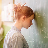 A woman rests her head against a chalkboard. She has been defeated by test anxiety.