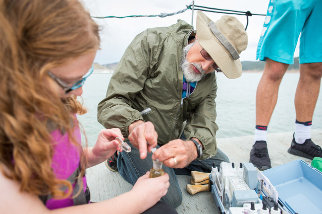 A young woman and a professor look at a collected vial. They are on a boat.