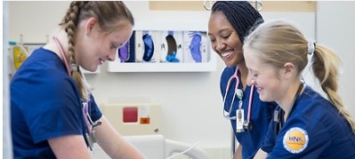 Three nursing students wearing blue scrubs in a clincial classroom