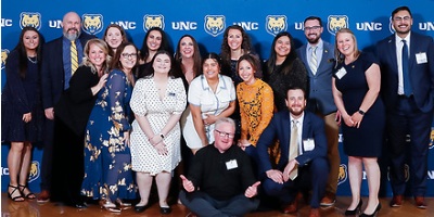 A group of 17 alumni in dressy clothes posing for a photo at the Honored Alumni event