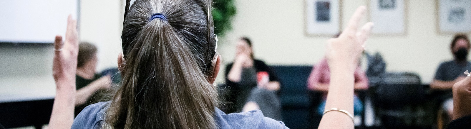 A group of individuals sitting in a circle, shot from behind an individual's shoulder