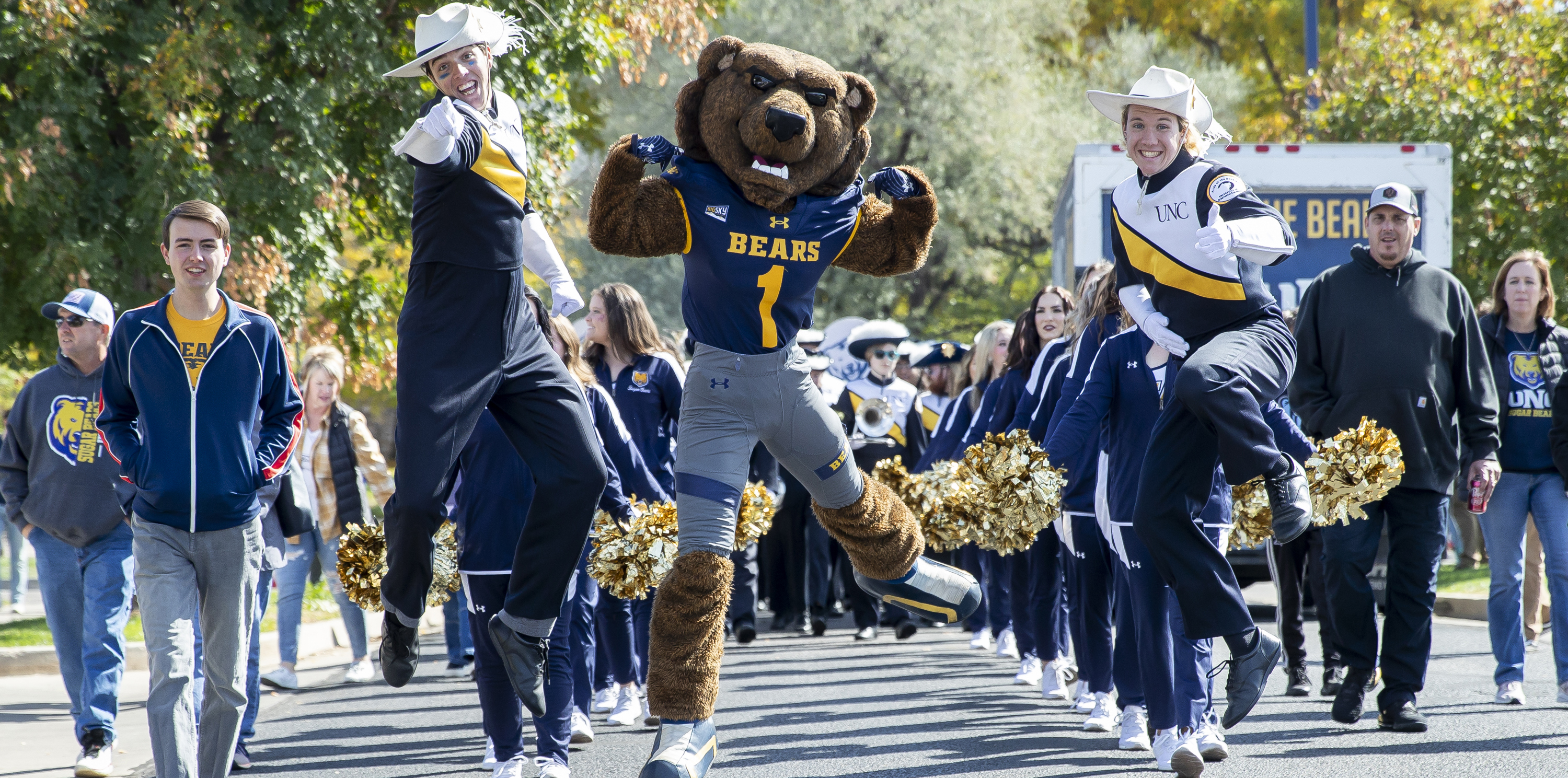 Klawz and two members from UNC's marching band jumping in the air while the band marches down a street.