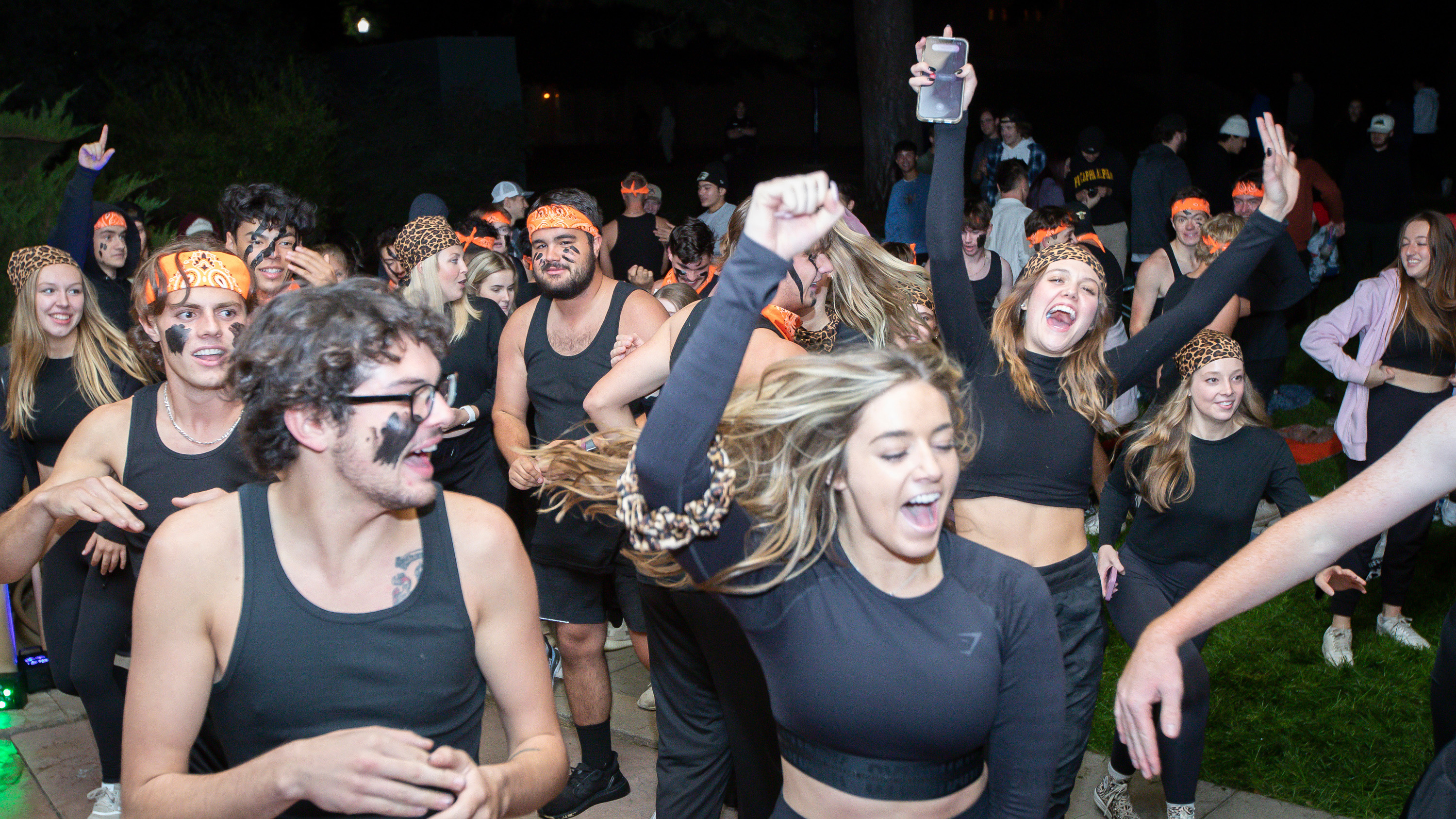 Fraternity and sorority members dressed in black and orange dancing together