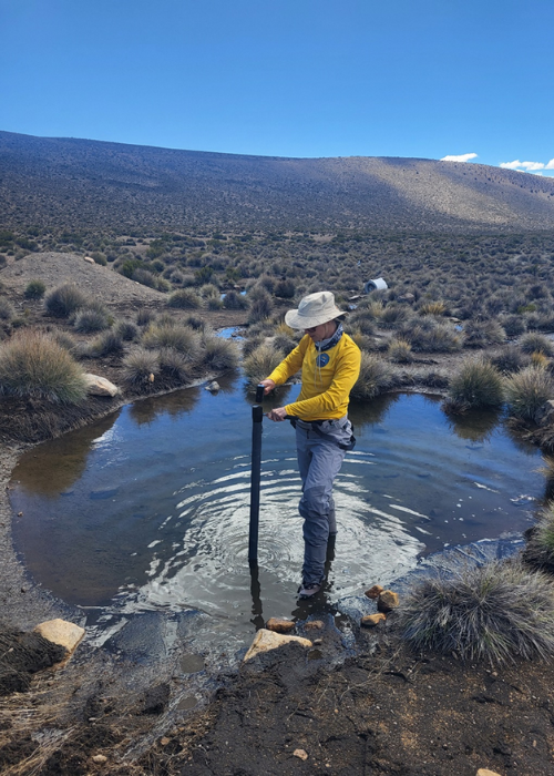 A person in a yellow shirt, standing in a puddle with a scientific measuring instrument