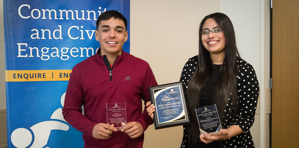 Male and female student standing up while smiling and holding awards
