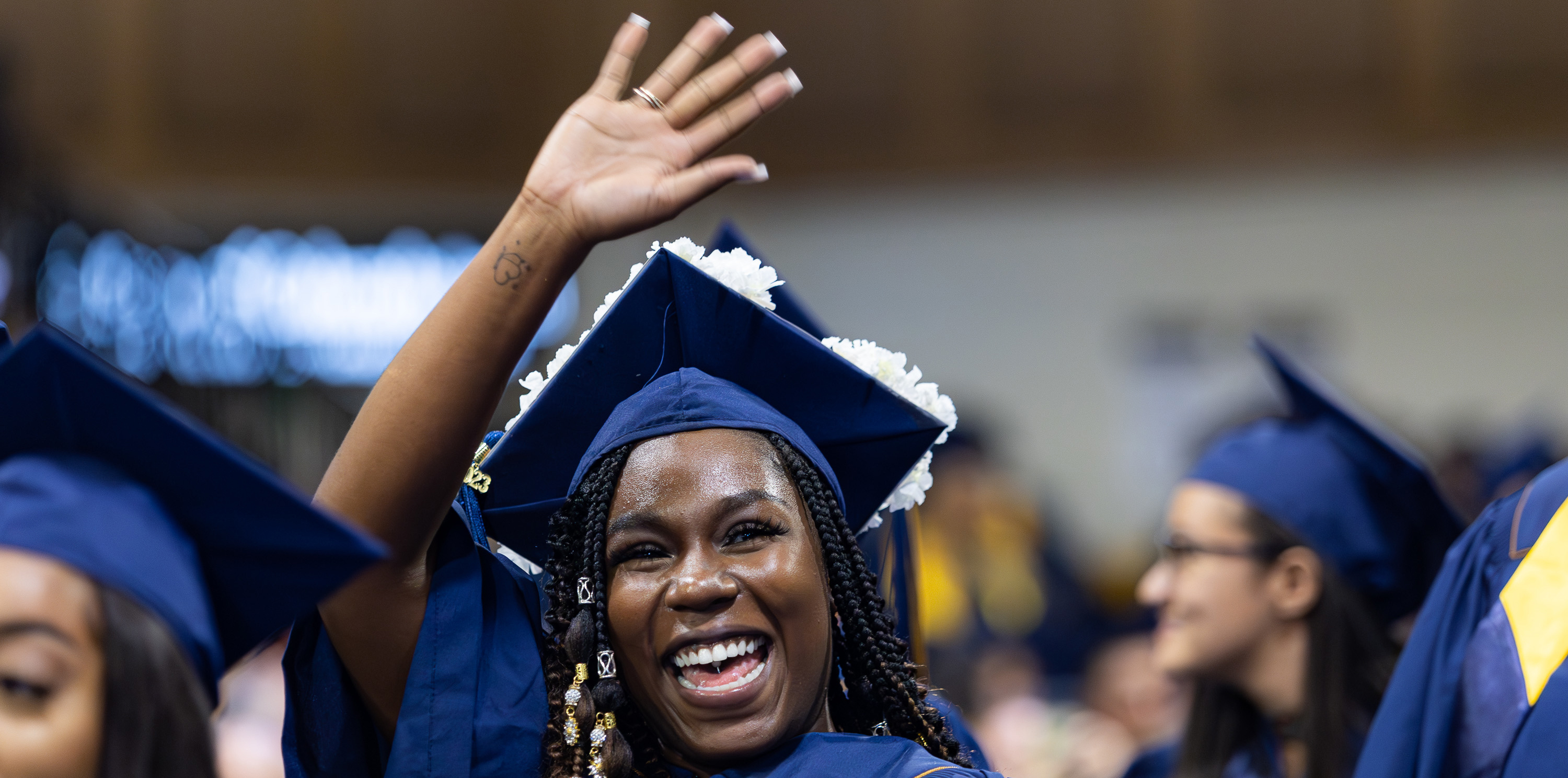 Female college student in her cap and gown at graduation, smiling and waving