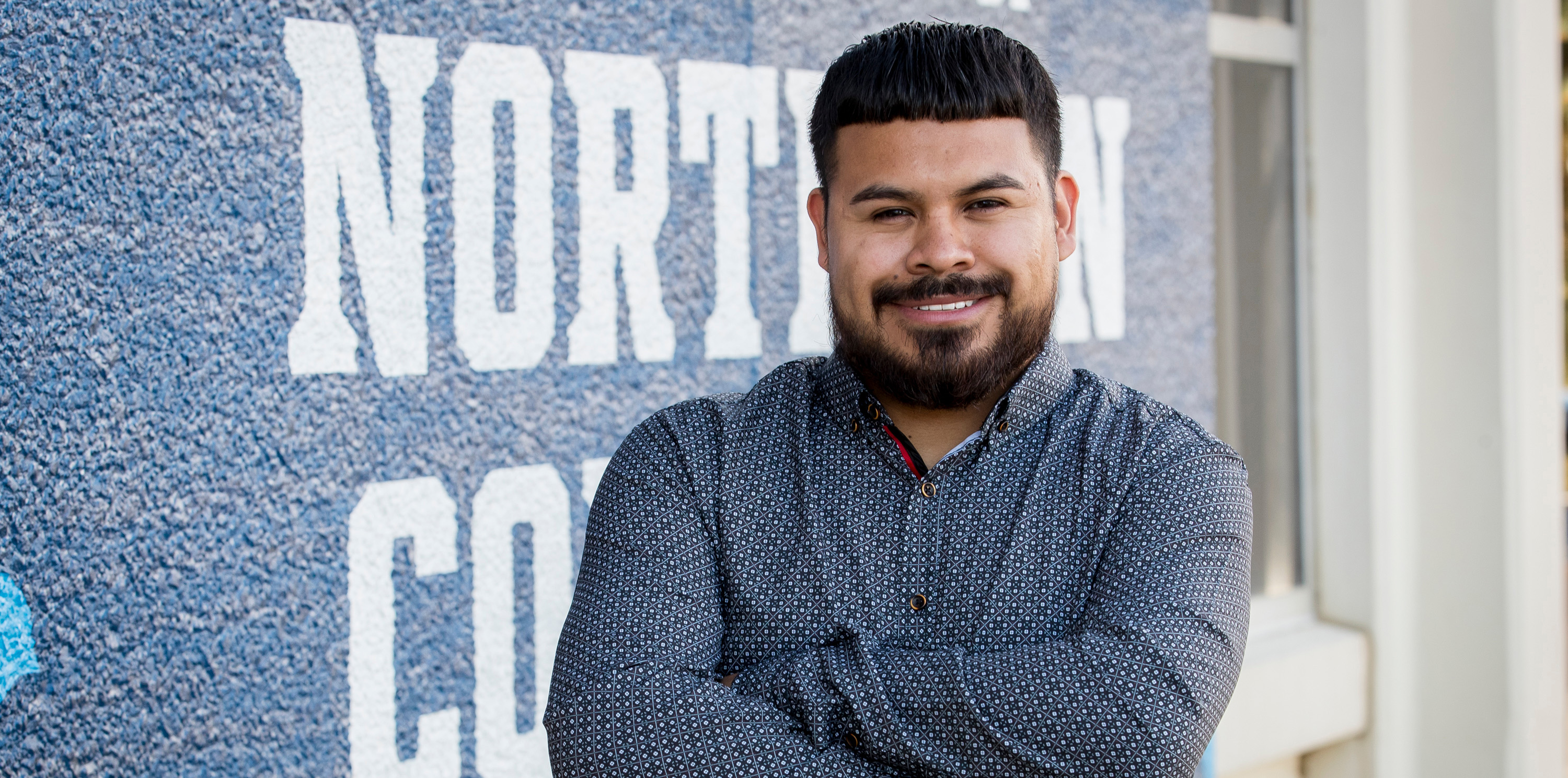 Fernando standing against a wall with his arms crossed smiling