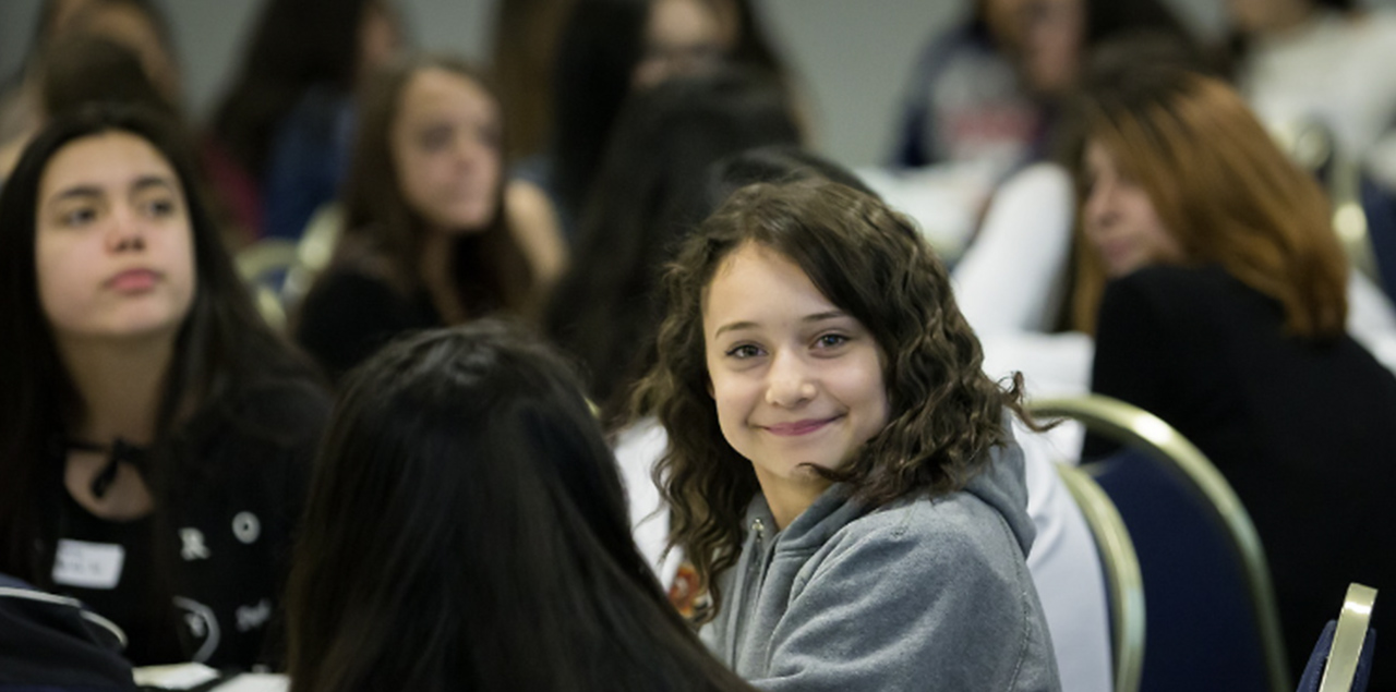 A young student attending to the Latina Youth Leadership Conference smiling 