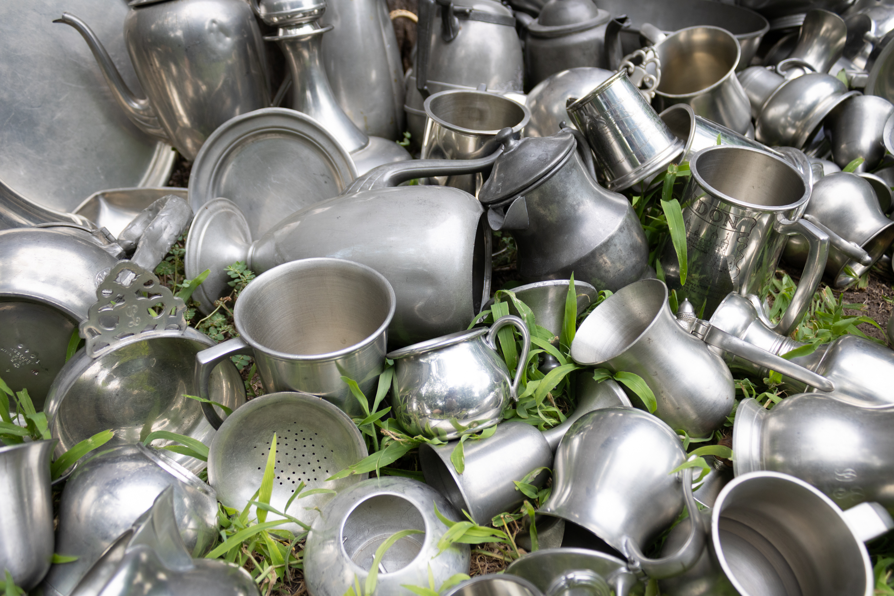 A variety of pewter mugs, cups and other items sitting in a grass field.