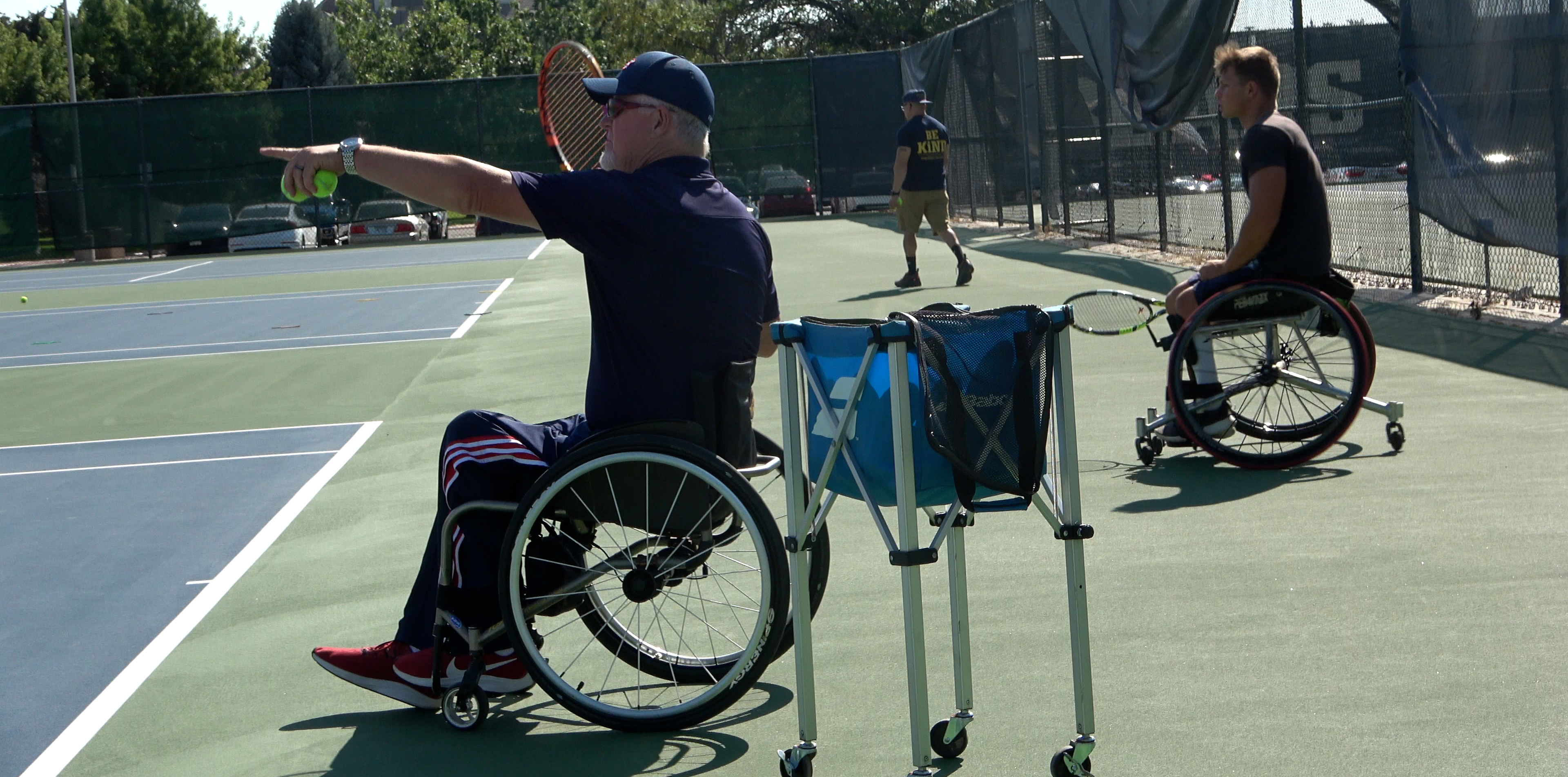 Scott Douglas coaching wheelchair tennis holding up his arm and pointing
