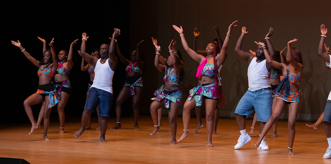 A group of dancers on a stage mid dance with their right arms up