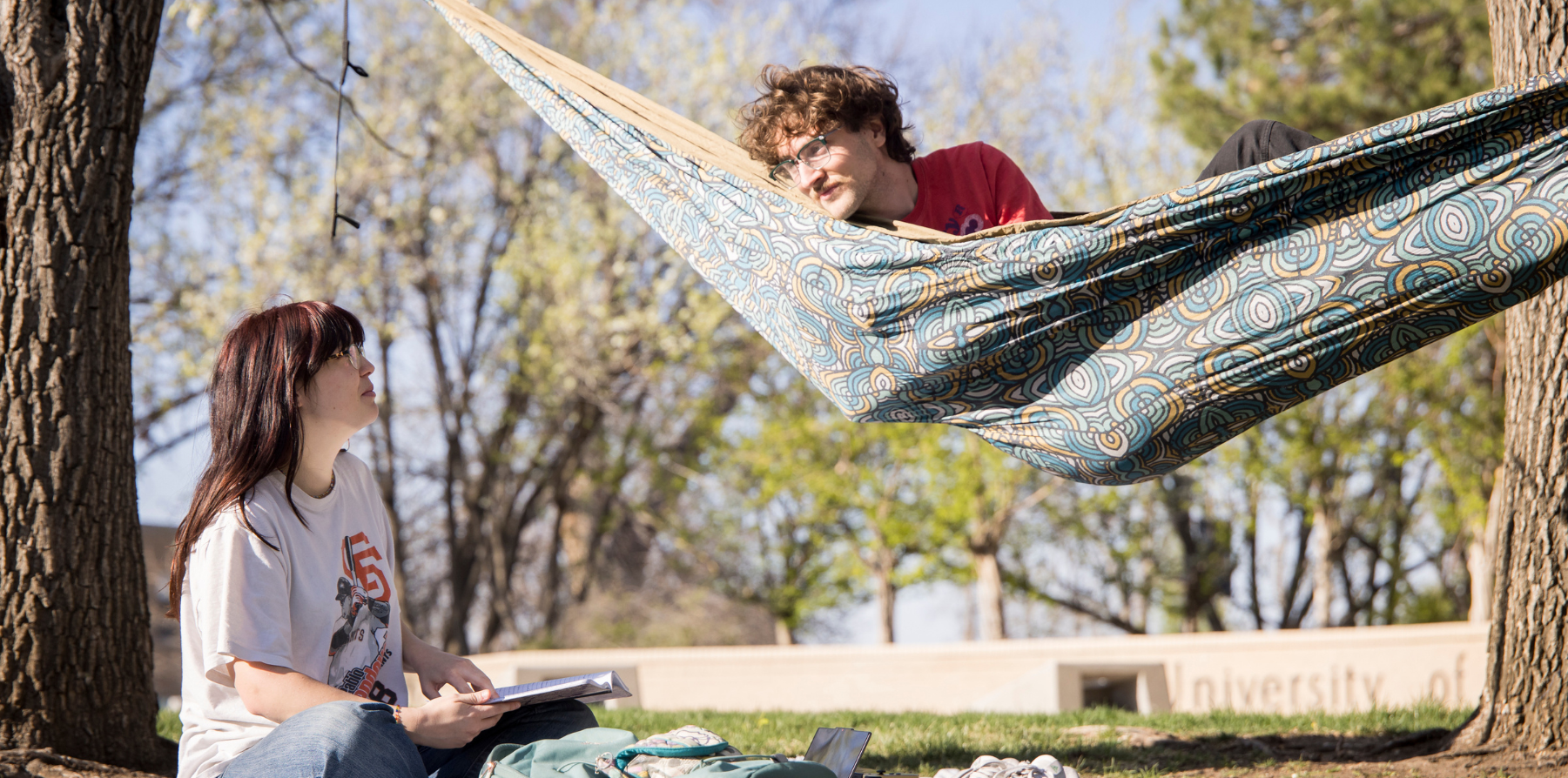 Two students relaxing on campus, one in a hammock.