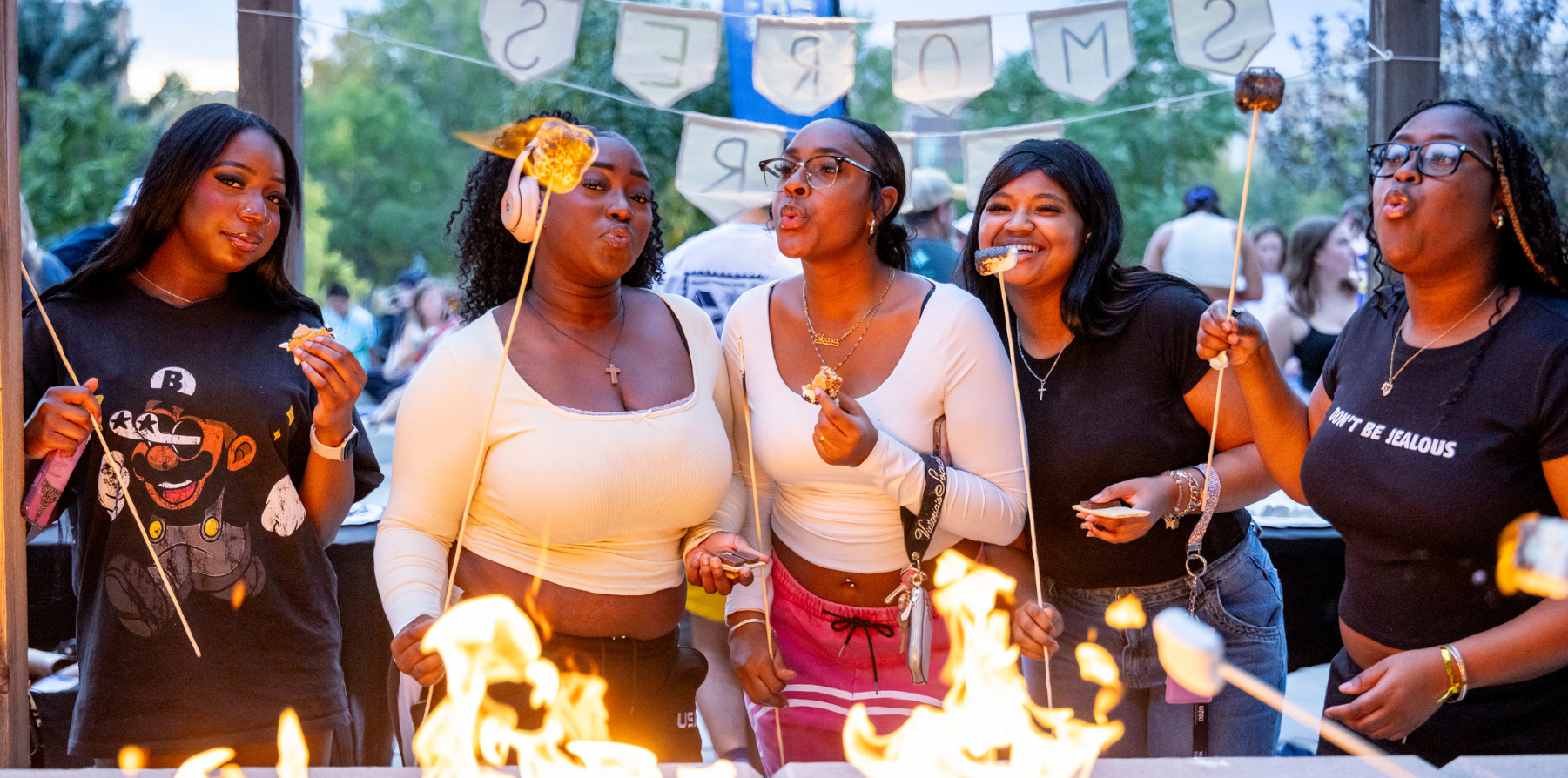 Three students roasting marshmallows over a bonfire out front of the University Center.