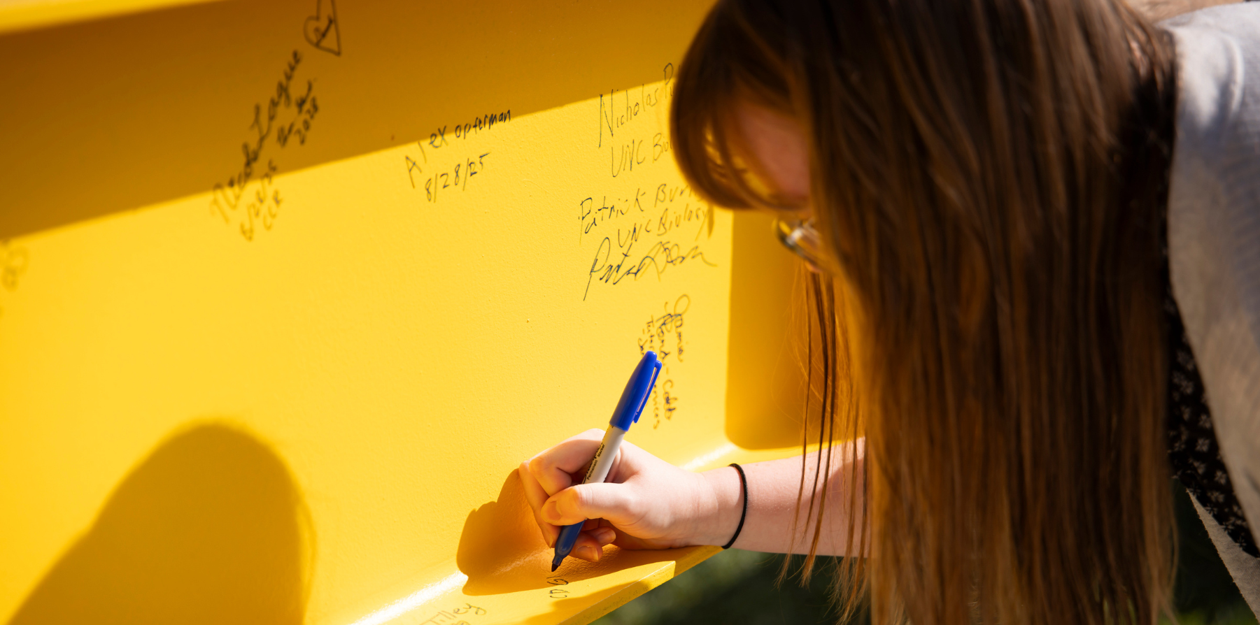 A student signing a yellow contruction beam with a sharpie.