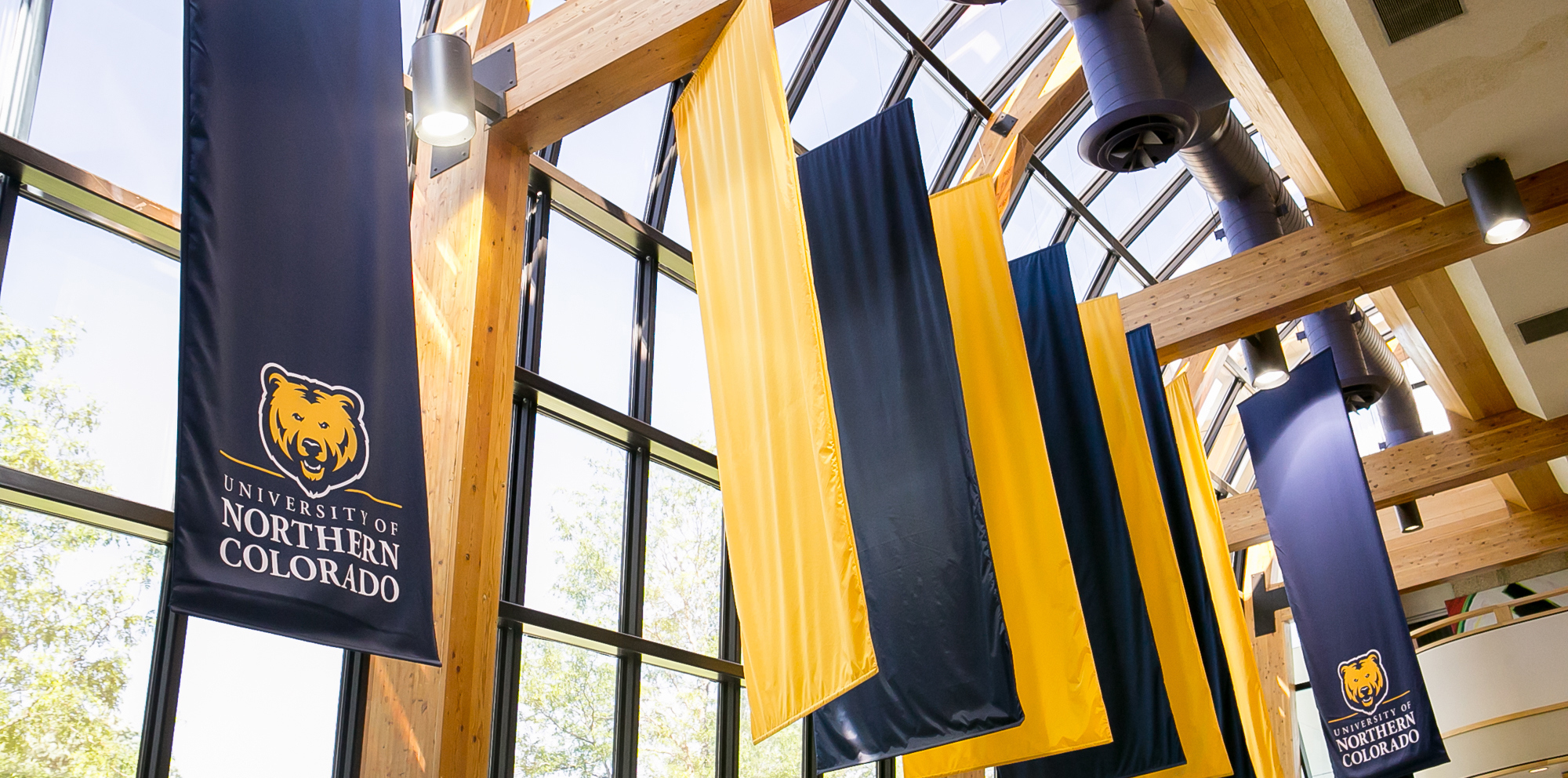 Blue and gold banners hanging from the ceiling of the university center against a backdrop of windows