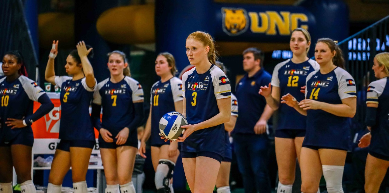 Syd Cole stands with a volleyball in her hands while a row of her teammates stand behind her.