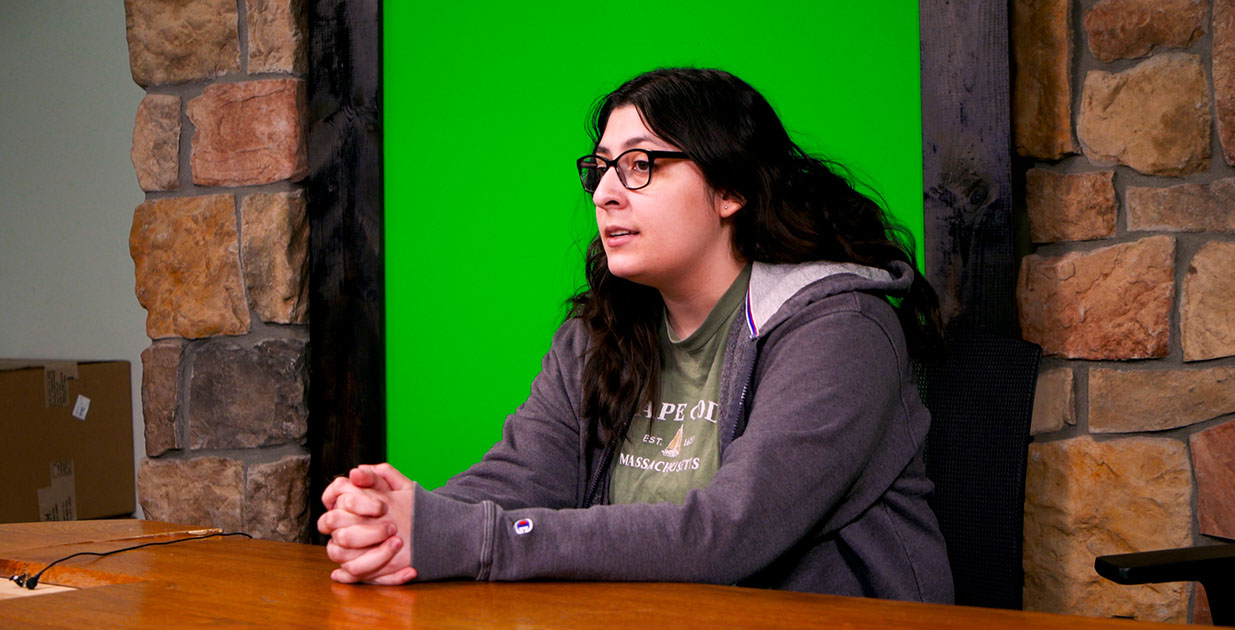 Zvi Gutierrez sitting at a desk with a green screen behind her